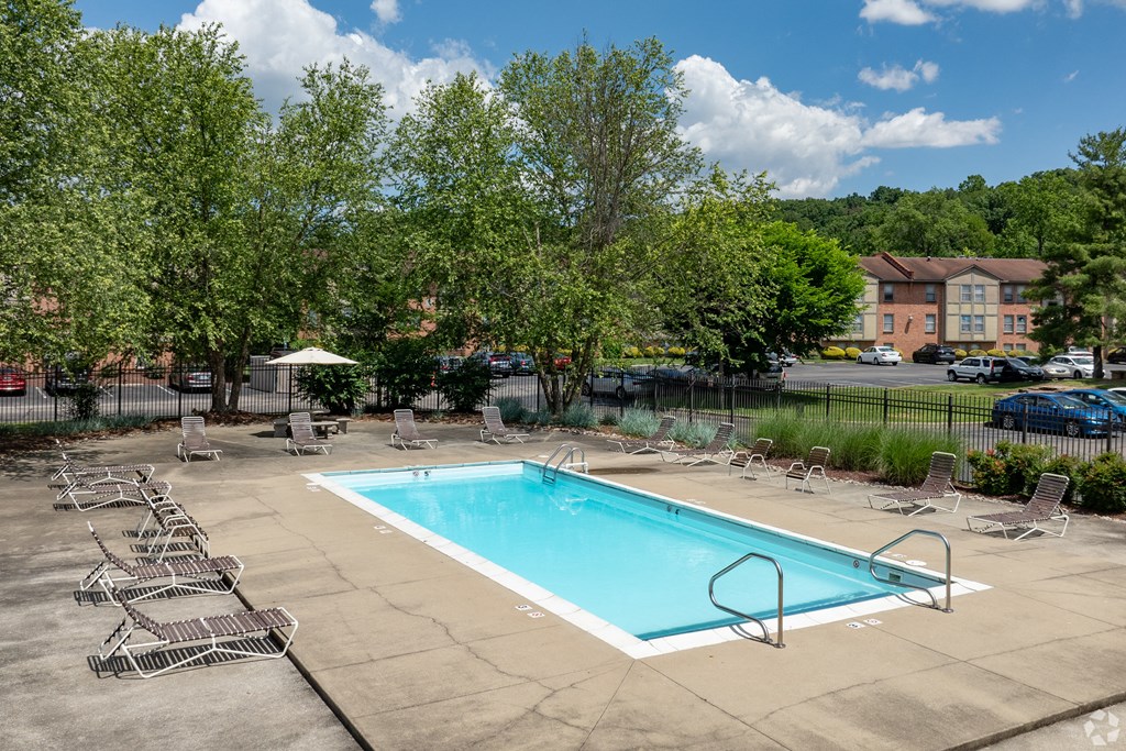 a swimming pool with chairs and trees and a building in the background