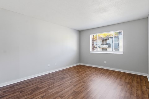 A room with wooden flooring and a window showing a building outside.