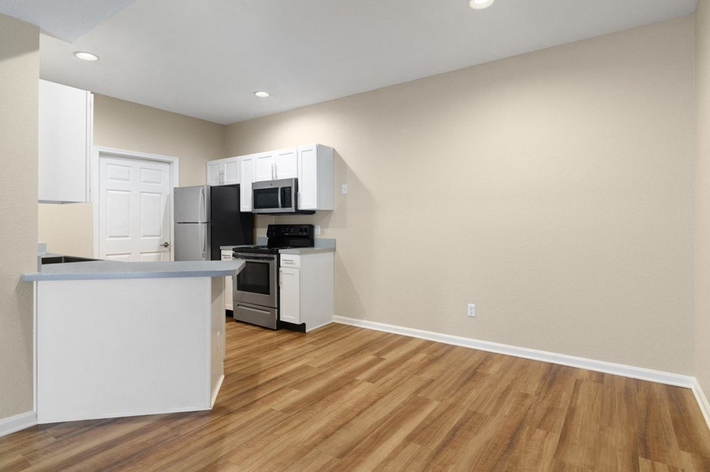 an empty kitchen with a hard wood floor and white cabinets