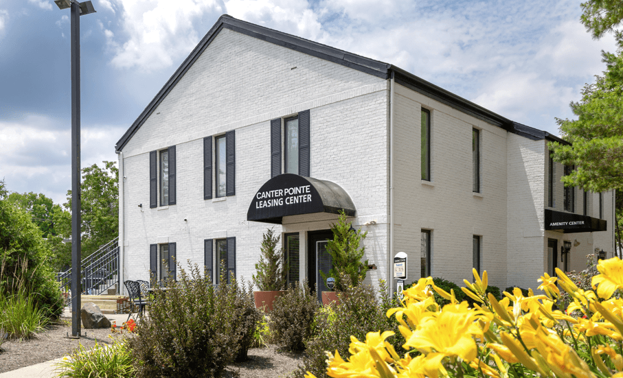 a white building with a black and white sign and yellow flowers