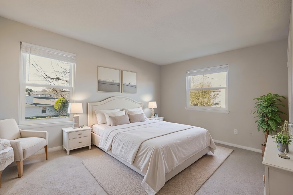 A bedroom with a large bed, a chair, and a potted plant.