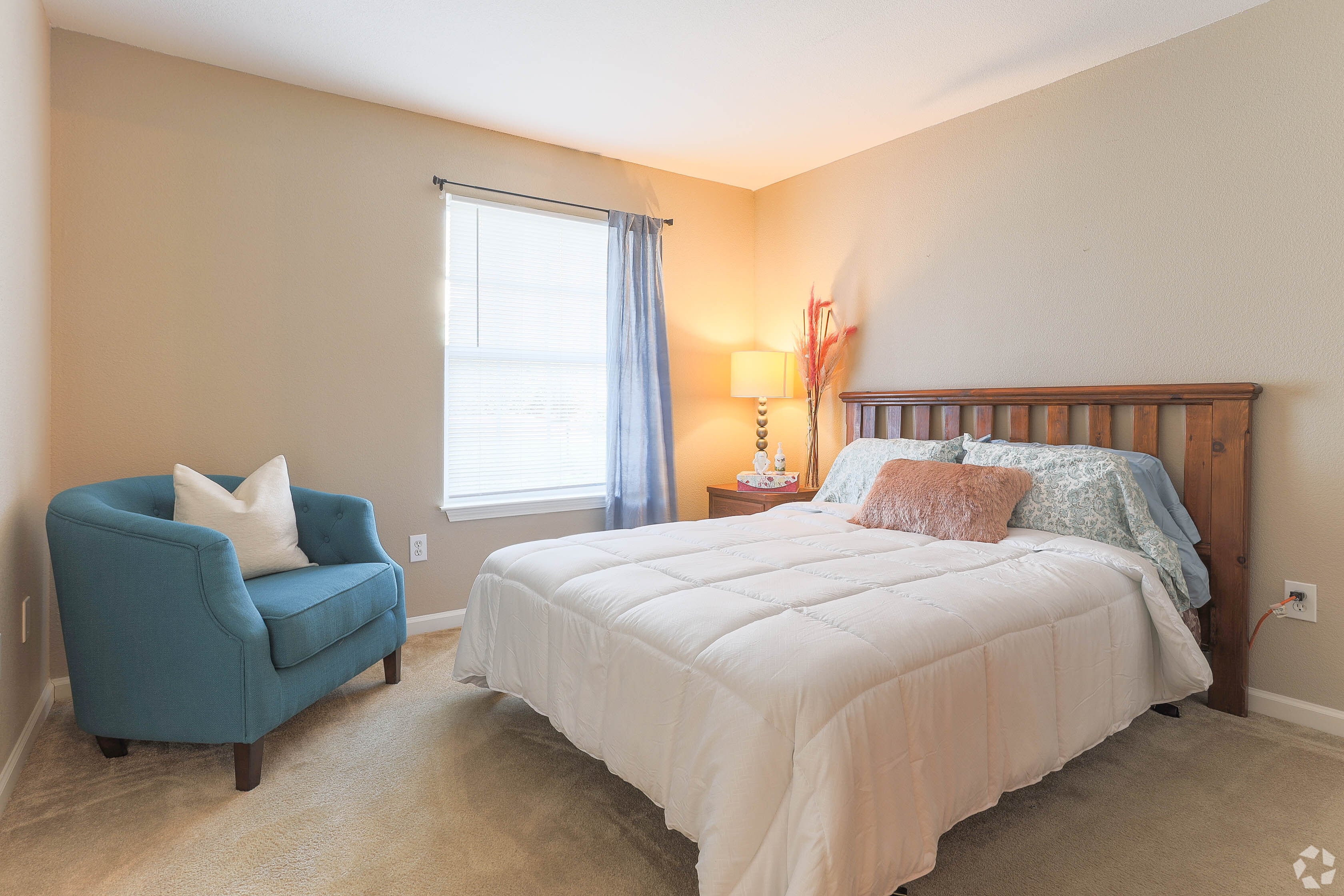 Bright, spacious bedroom with white bed and blue accent chair in an apartment home at Waterbrook Apartments in Lincoln, Nebraska, professionally operated by Highlands Vista Group.