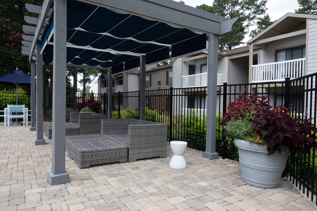 a pergola with a seating area and potted plants in front of an apartment complex