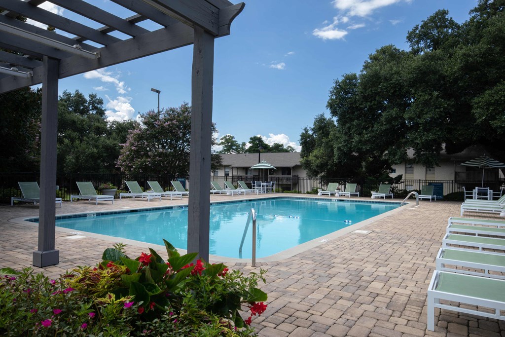 a swimming pool with chaise lounge chairs and trees in the background