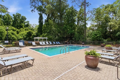 A sparkling swimming pool at Aspen Run Apartments surrounded by lounge chairs and lush trees.