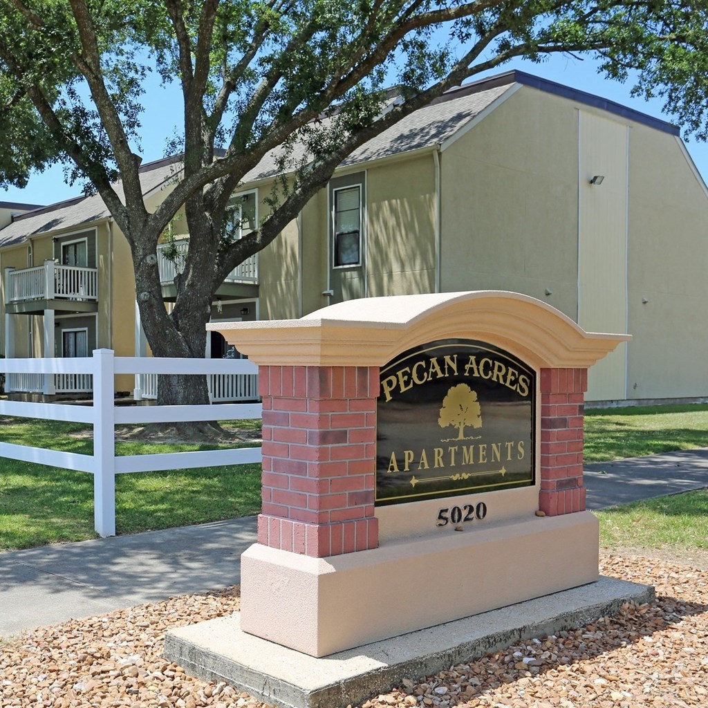 a sign for pecan acres apartments in front of a white fence
