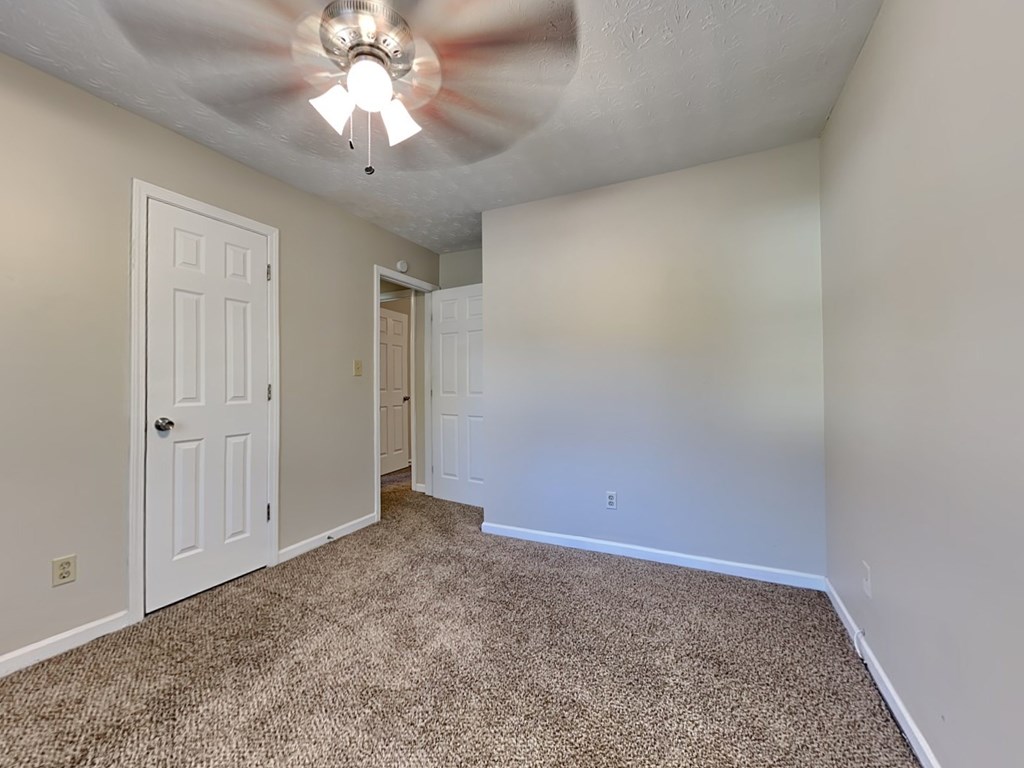 an empty living room with a ceiling fan and a white door