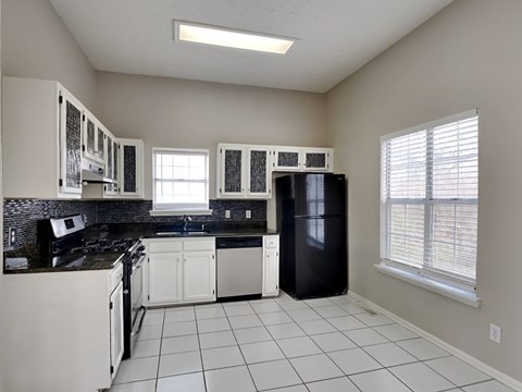 A kitchen with white cabinets and black countertops.