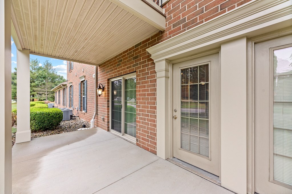 the front porch of a brick house with windows and a concrete sidewalk