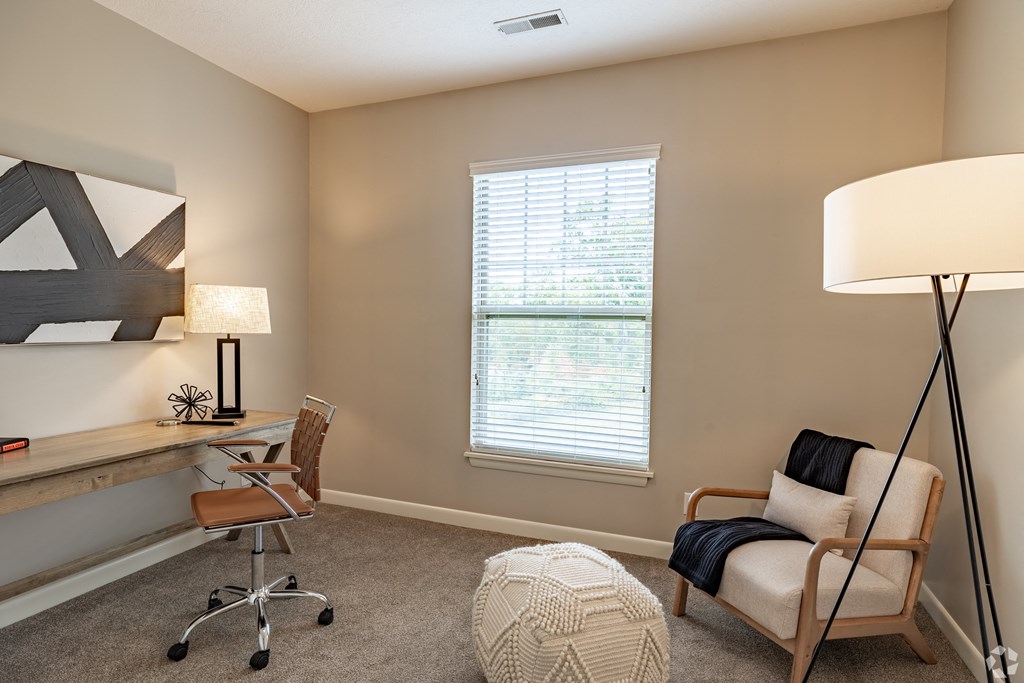 an office with a chair and a desk with a lamp and a window