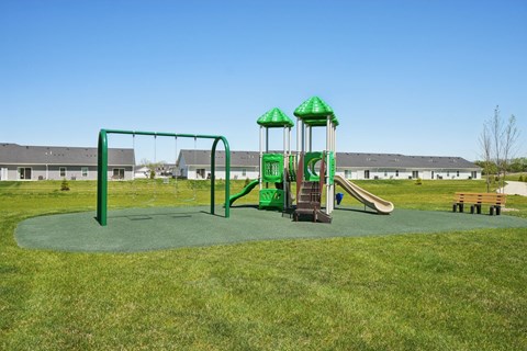A playground with a green swing set and a green and white slide.