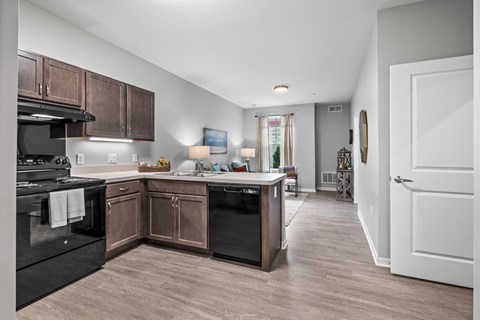 a kitchen with wooden cabinets and black appliances and a hallway to a living room