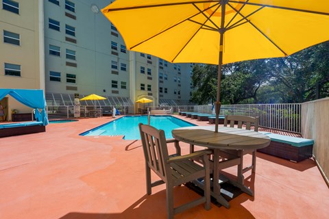 Resort style pool with patio seating and umbrellas at Landings of St. Andrew Apartments, Florida