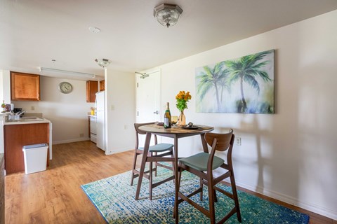 A dining room with a table and chairs and a painting of a palm tree on the wall.