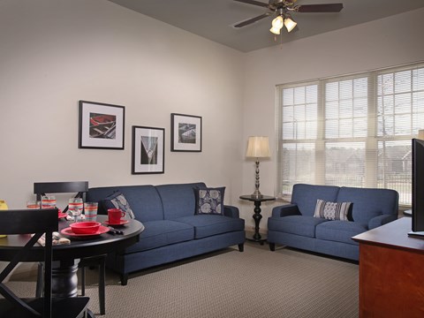 A living room with a blue couch, a black table, and a ceiling fan.