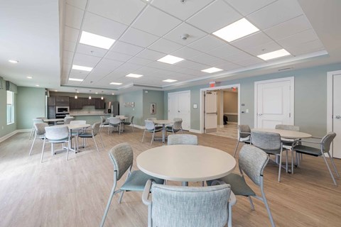 A room with tables and chairs and a kitchen area.