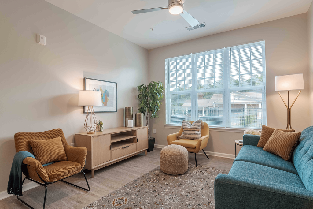 A living room with a blue couch, a chair, a table, and a ceiling fan at Sweetwater Point in Douglasville, GA.