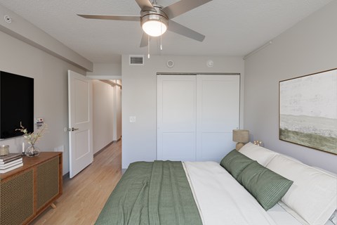 A bedroom with a bed, a ceiling fan, and a painting on the wall.