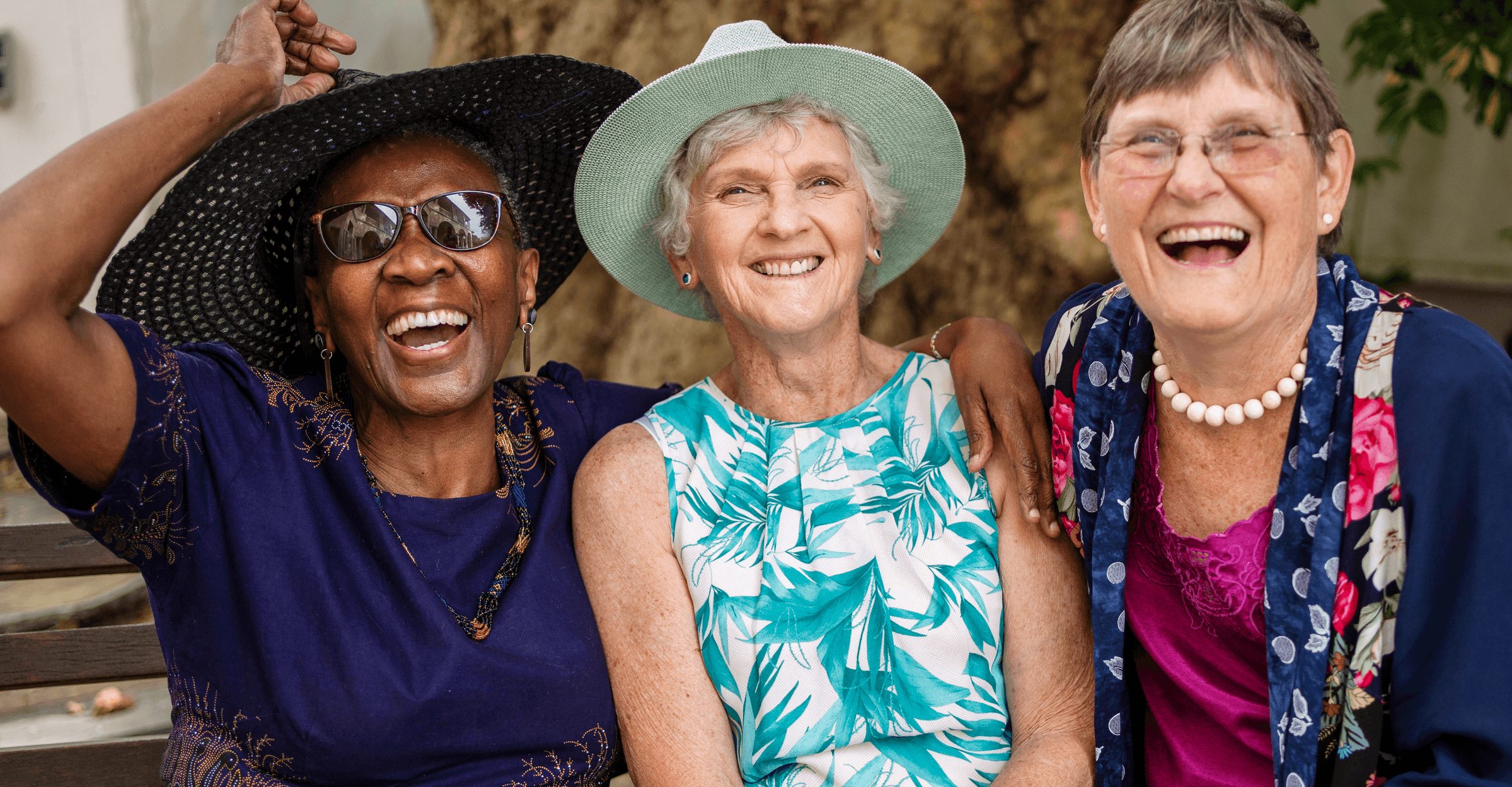 Three women are laughing together in front of a tree.