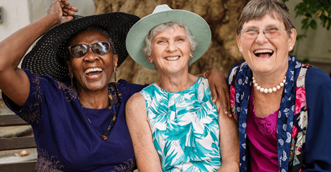 Three women are laughing together in front of a tree.