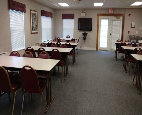 A room with tables and chairs and a TV on the wall.