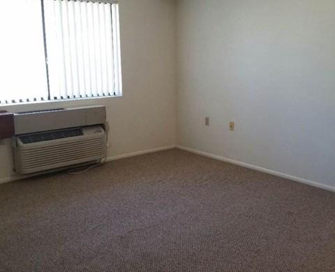A room with a carpeted floor and a window with blinds.