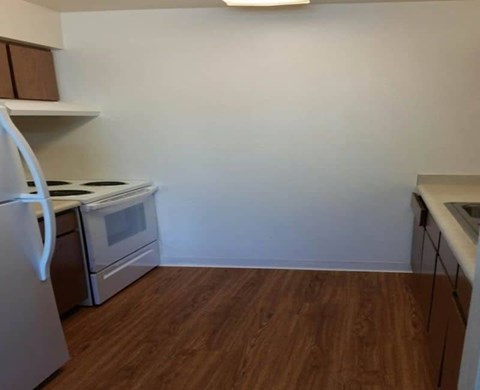 A kitchen with a white fridge, stove and oven, and a wooden floor.