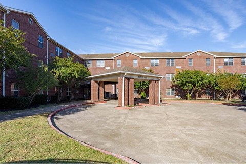 A parking lot in front of a brick building with a covered walkway.