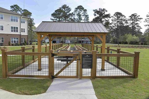 A wooden gazebo with a metal roof is surrounded by a fence and has a sign on it.