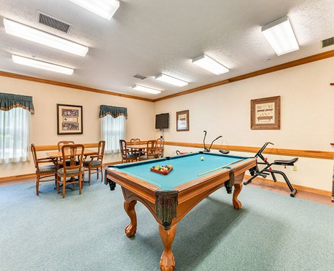 A pool table is in the middle of a room with chairs and pictures on the wall.