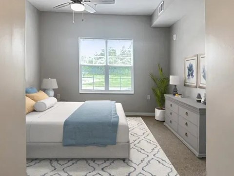 A bedroom with a bed, dresser, and window overlooking a green area.