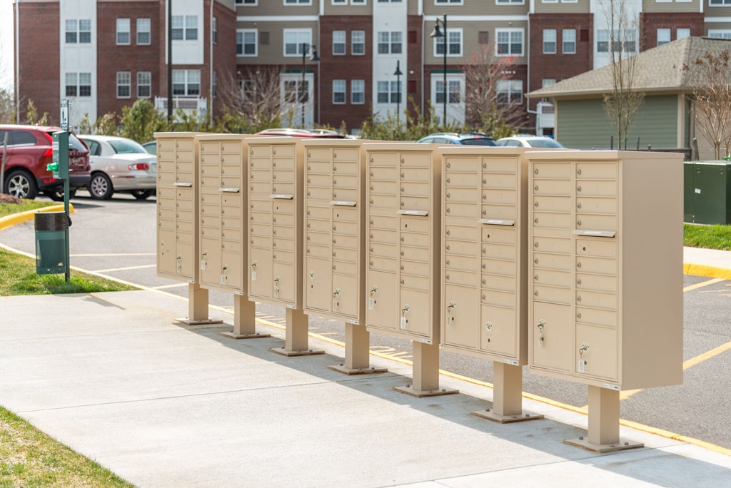 a row of mailboxes sit on a sidewalk in front of an apartment building at The Whitworth, Williamsburg, 23185