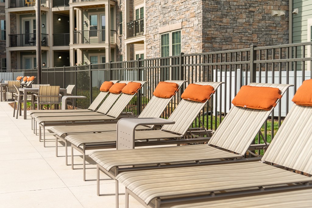 a row of lounge chairs with orange pillows in front of an apartment building at The Whitworth, Williamsburg, 23185