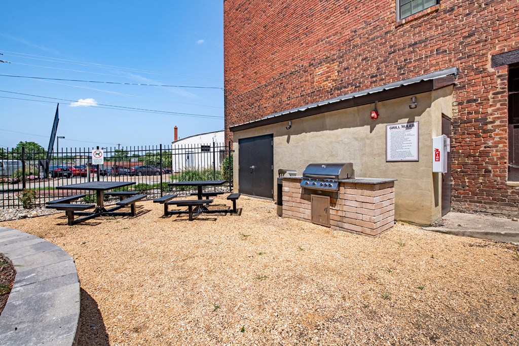 a picnic area outside of a brick building with a grill and picnic table at Mayton Transfer Lofts in Petersburg, VA