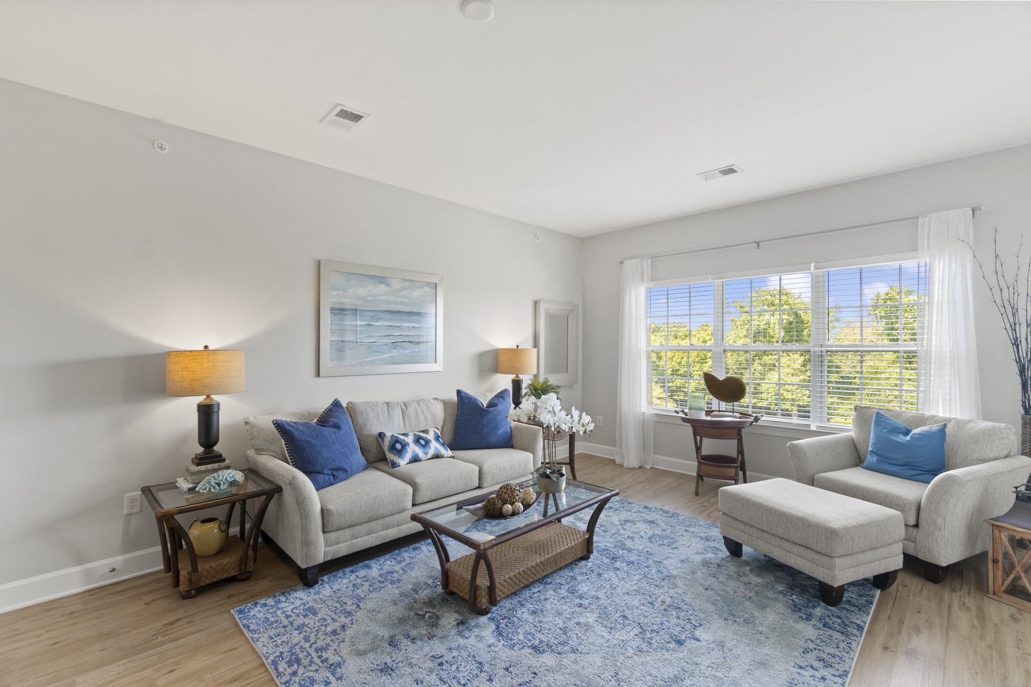 A living room with a grey couch, a blue rug, and a painting on the wall.
