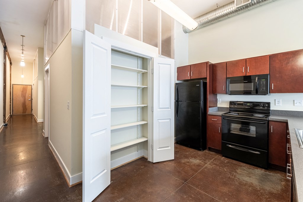 a kitchen with a black refrigerator and black appliances and a white closet with open doors at Mayton Transfer Lofts in Petersburg, Virginia 23803