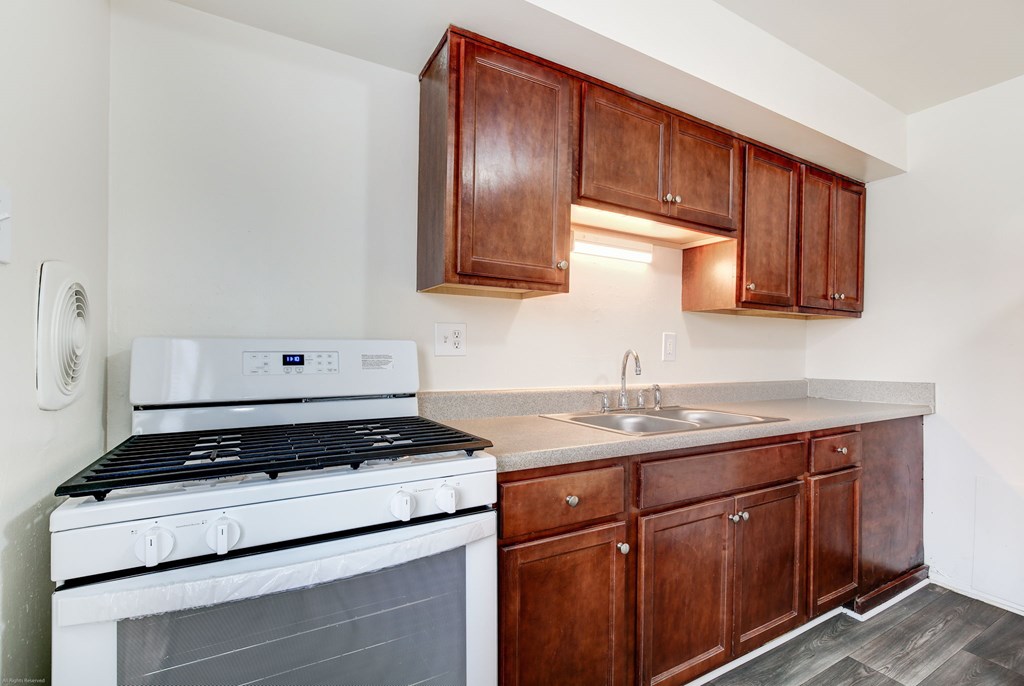 A white stove and sink in a kitchen with wooden cabinets.