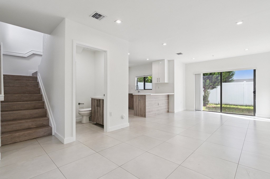 A spacious, white-walled room with a staircase on the left and a sliding glass door on the right.at The Villages at Miami Gardens, Miami Gardens Florida