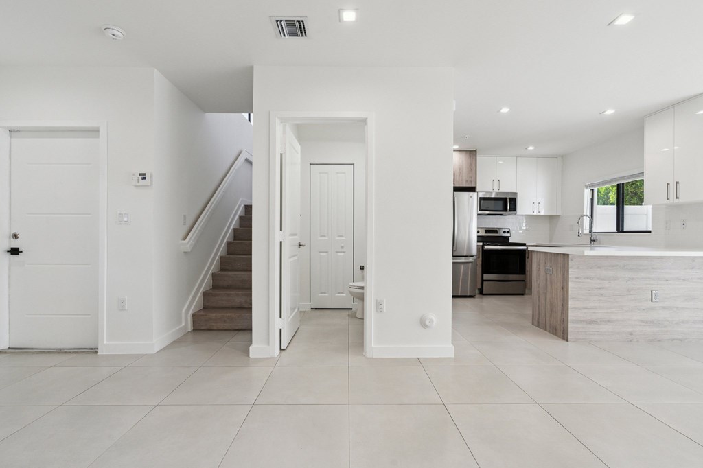 A white interior of a house with a kitchen and a staircase.at The Villages at Miami Gardens, Miami Gardens, FL 33056