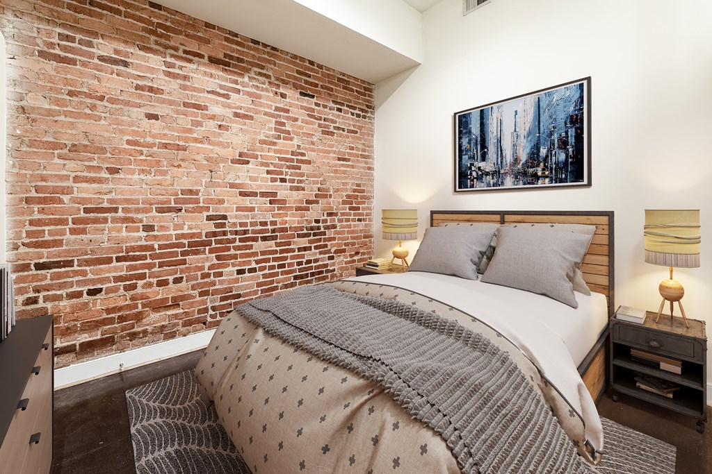 a bedroom with a bed and an exposed brick wall at Mayton Transfer Lofts in Petersburg, VA 23803