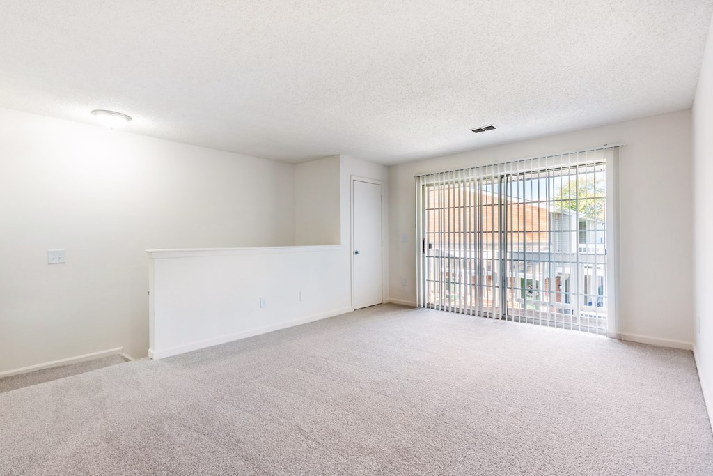 A white room with a carpeted floor and a sliding glass door leading to a balcony.