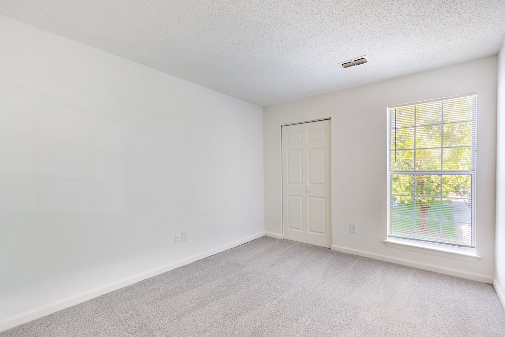 A room with a carpeted floor, a door, and a window.