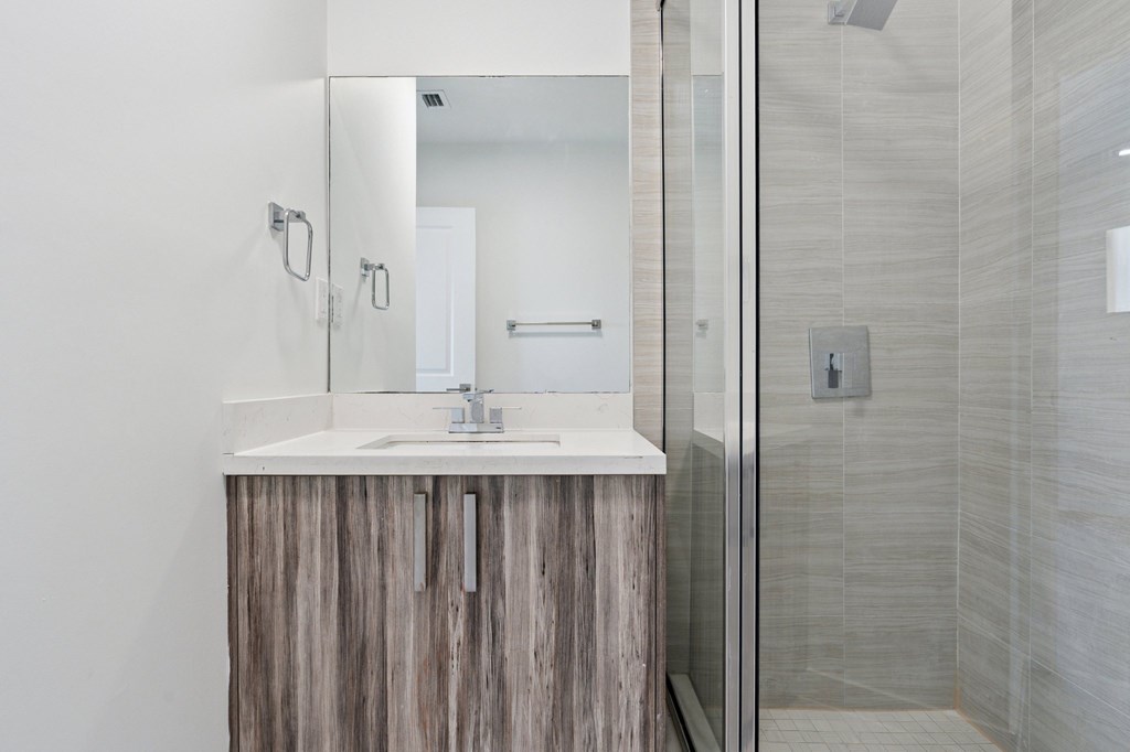 A bathroom with a wooden vanity and a glass shower door.at The Villages at Miami Gardens, Florida