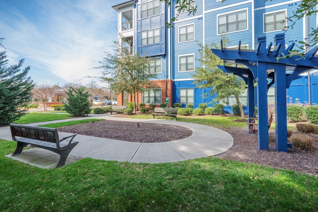 A park area with a bench and a tree in front of a blue building at Streets of Greenbrier, Chesapeake, 23320