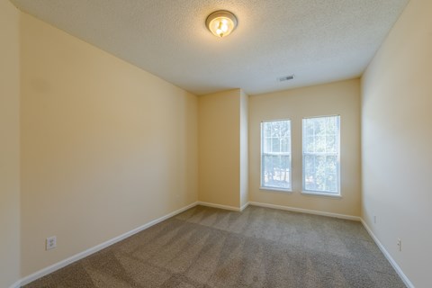 A room with a carpeted floor and a window with a view of trees.