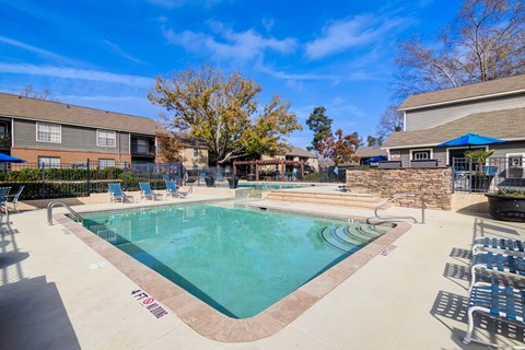 A pool surrounded by chairs and trees.