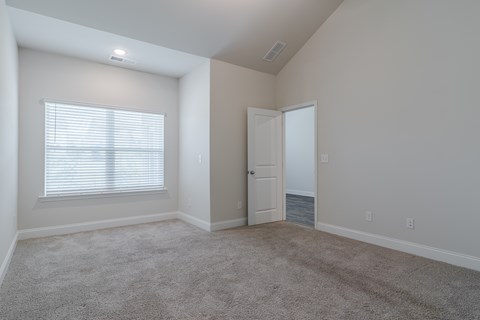 A room with a carpeted floor, a door, and a window with blinds.