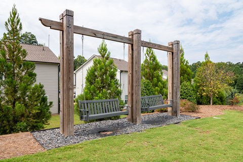 A wooden swing set in a grassy area with a house in the background.