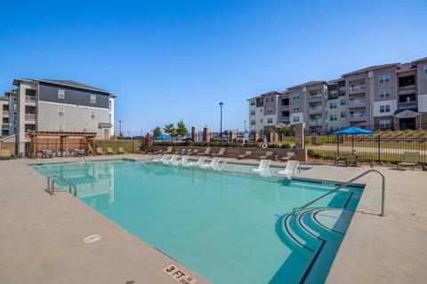 A large swimming pool with lounge chairs and apartment buildings in the background.
