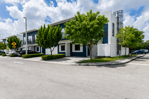 A modern building with a white and blue exterior is surrounded by trees and a clear sky.